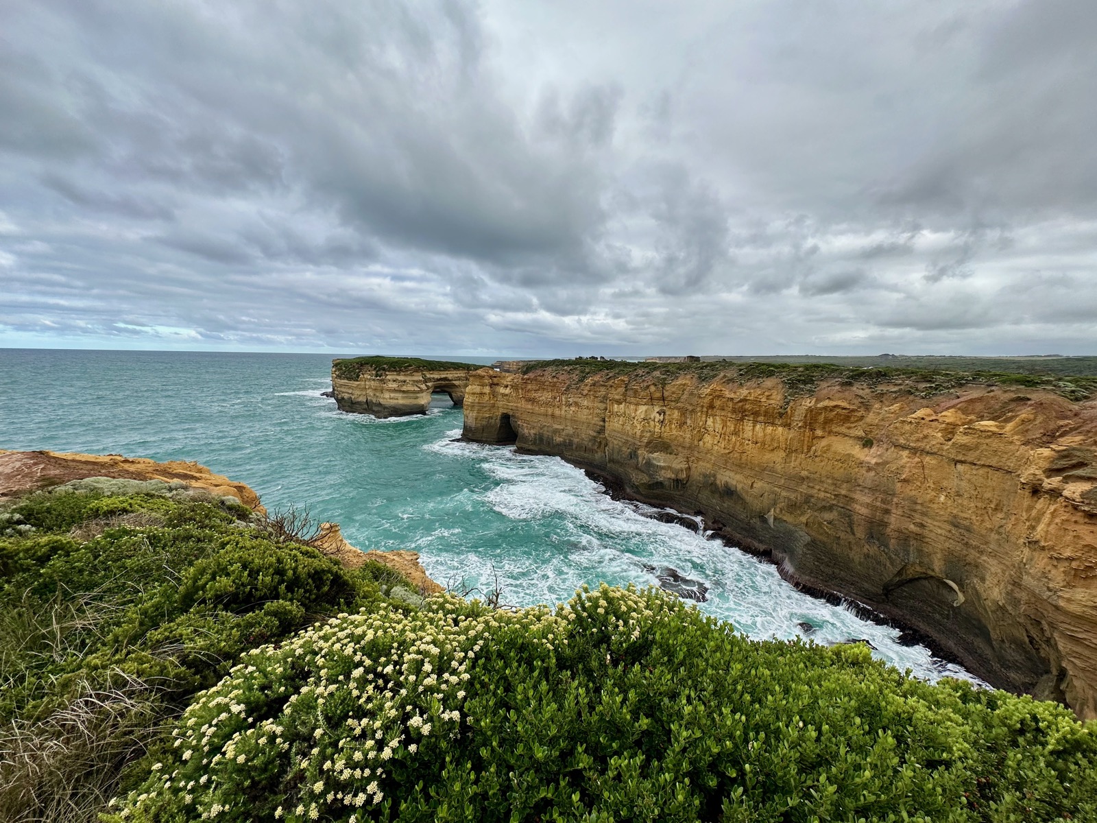 Cliffs with arches and waves crashing against them under a cloudy sky.